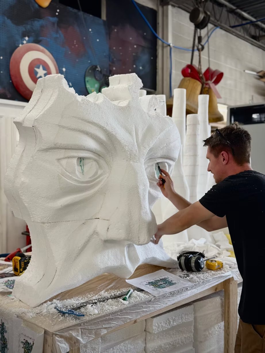 A sculptor detailing the eye of a giant carved foam face in the shop