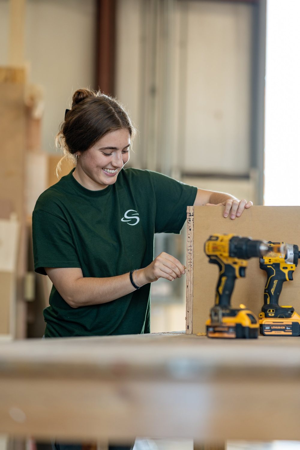 A smiling carpenter fastening a wooden panel, drills on the bench