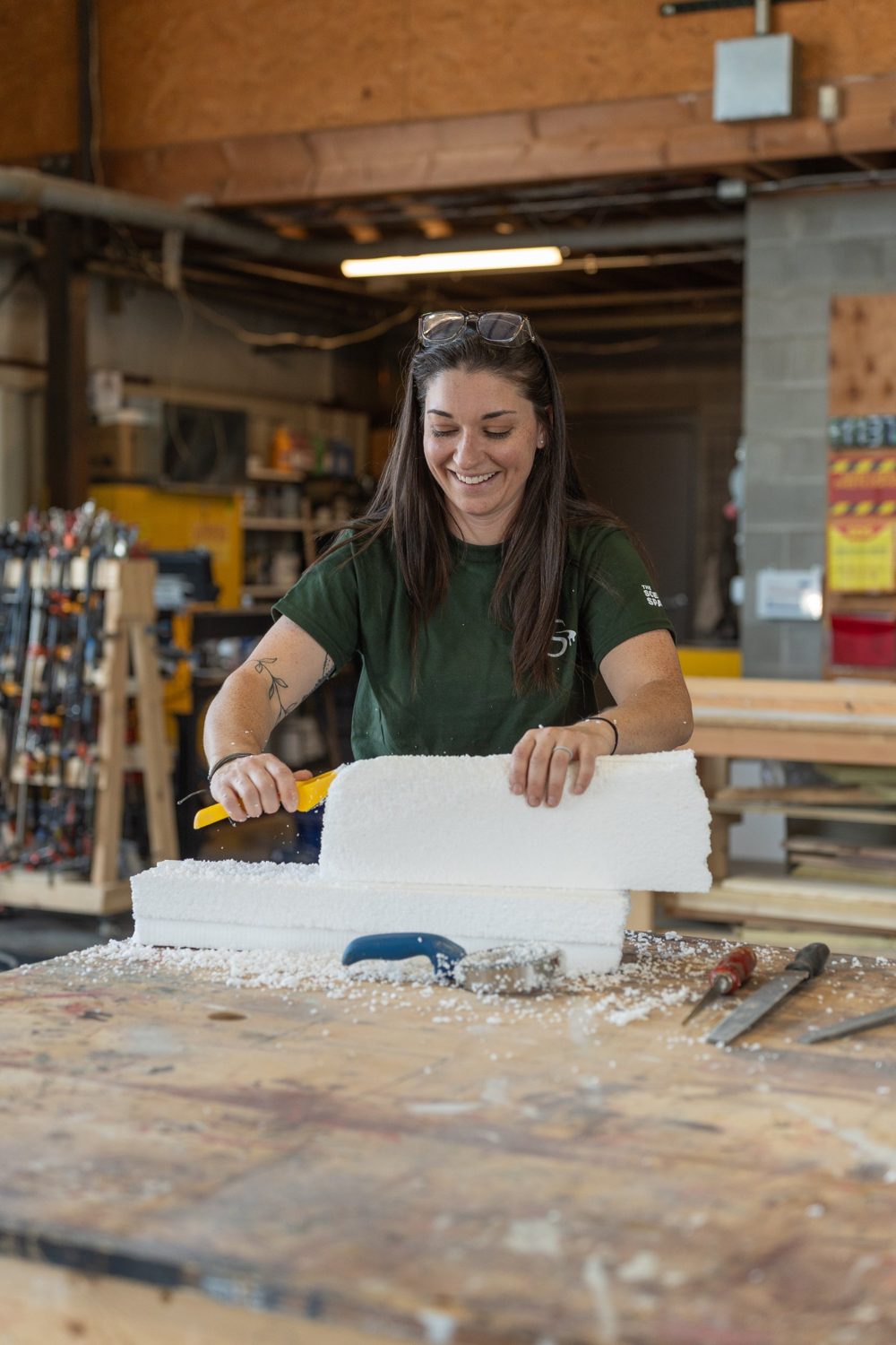 A smiling fabricator rasping a block of white foam into shape