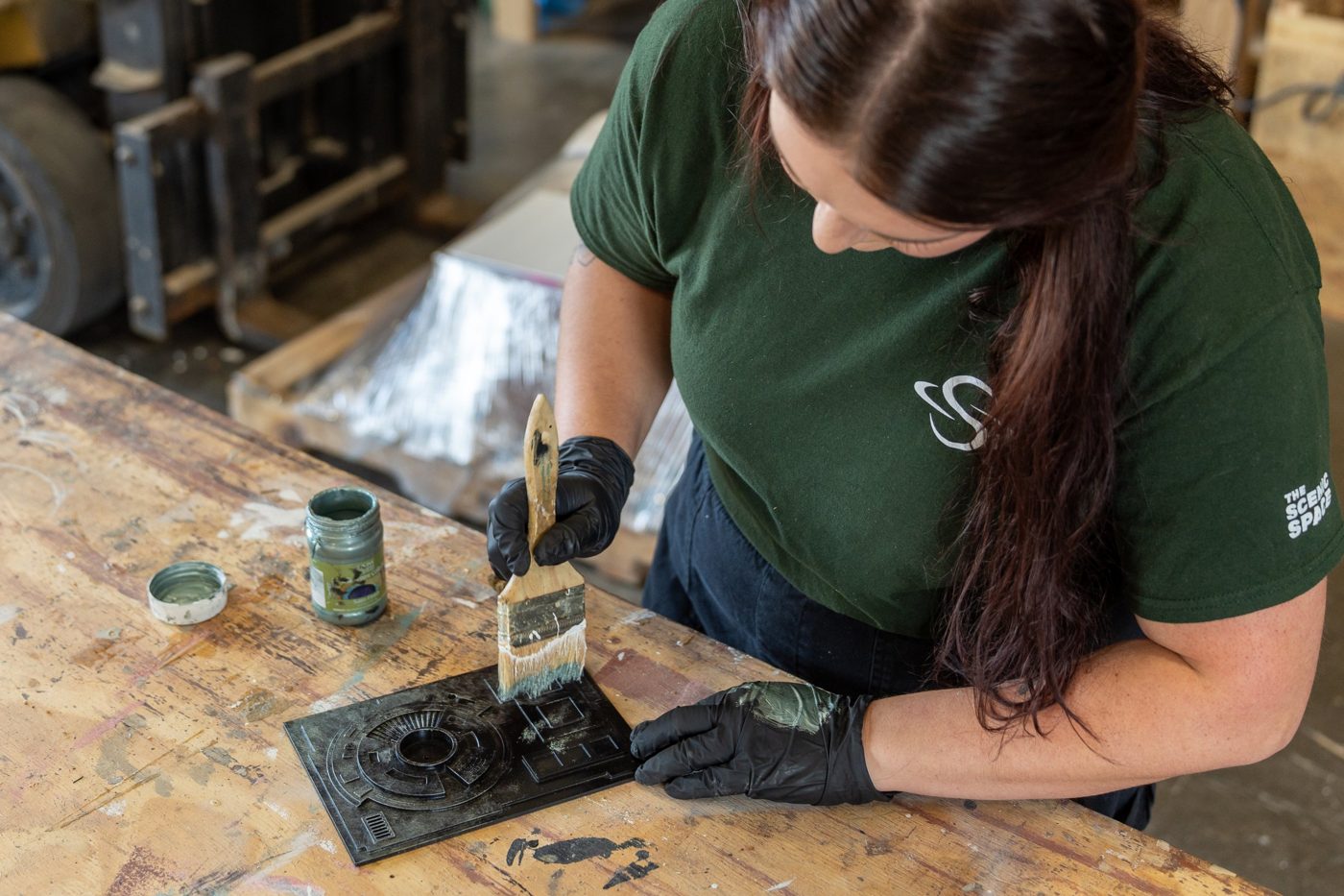 A scenic artist dry-brushing a metallic finish onto a black sci-fi panel