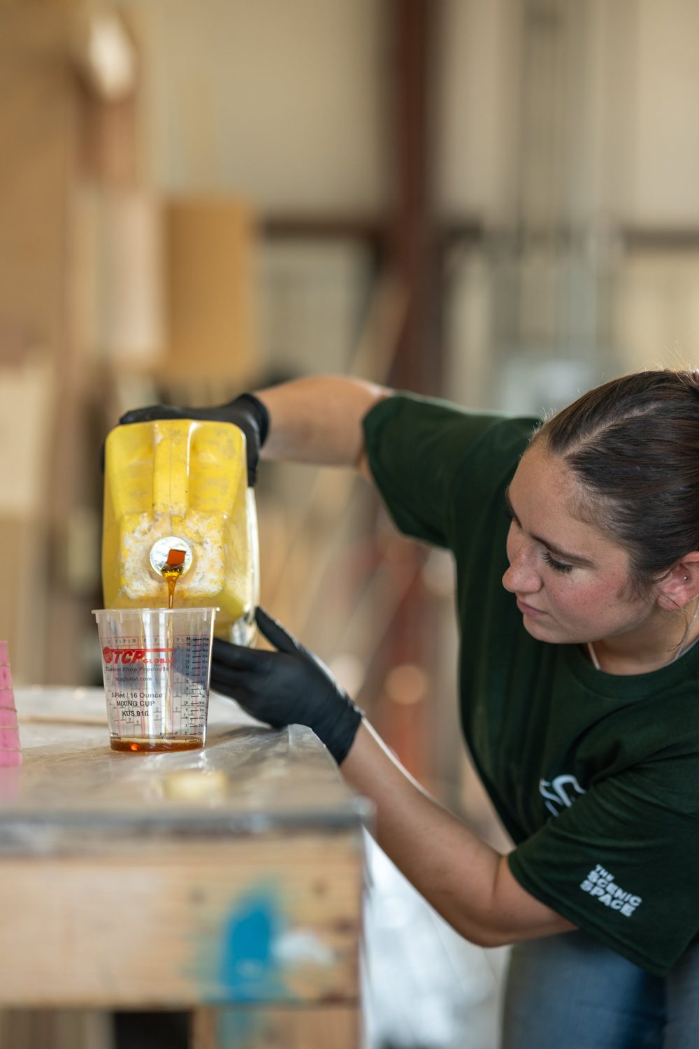 A fabricator in gloves pouring amber resin into a mixing cup