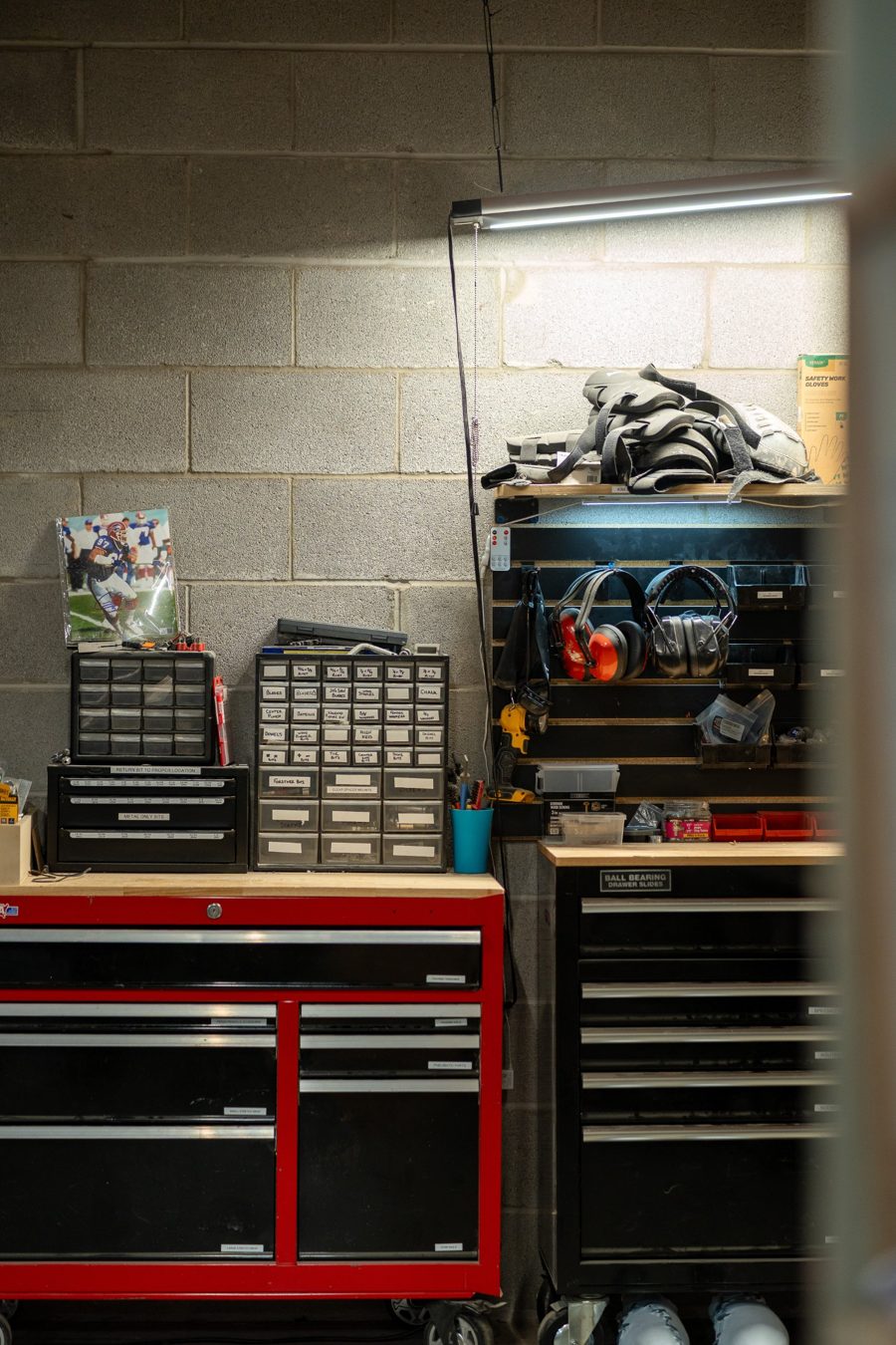 Red and black rolling tool chests with labeled parts drawers and ear protection on a slat wall