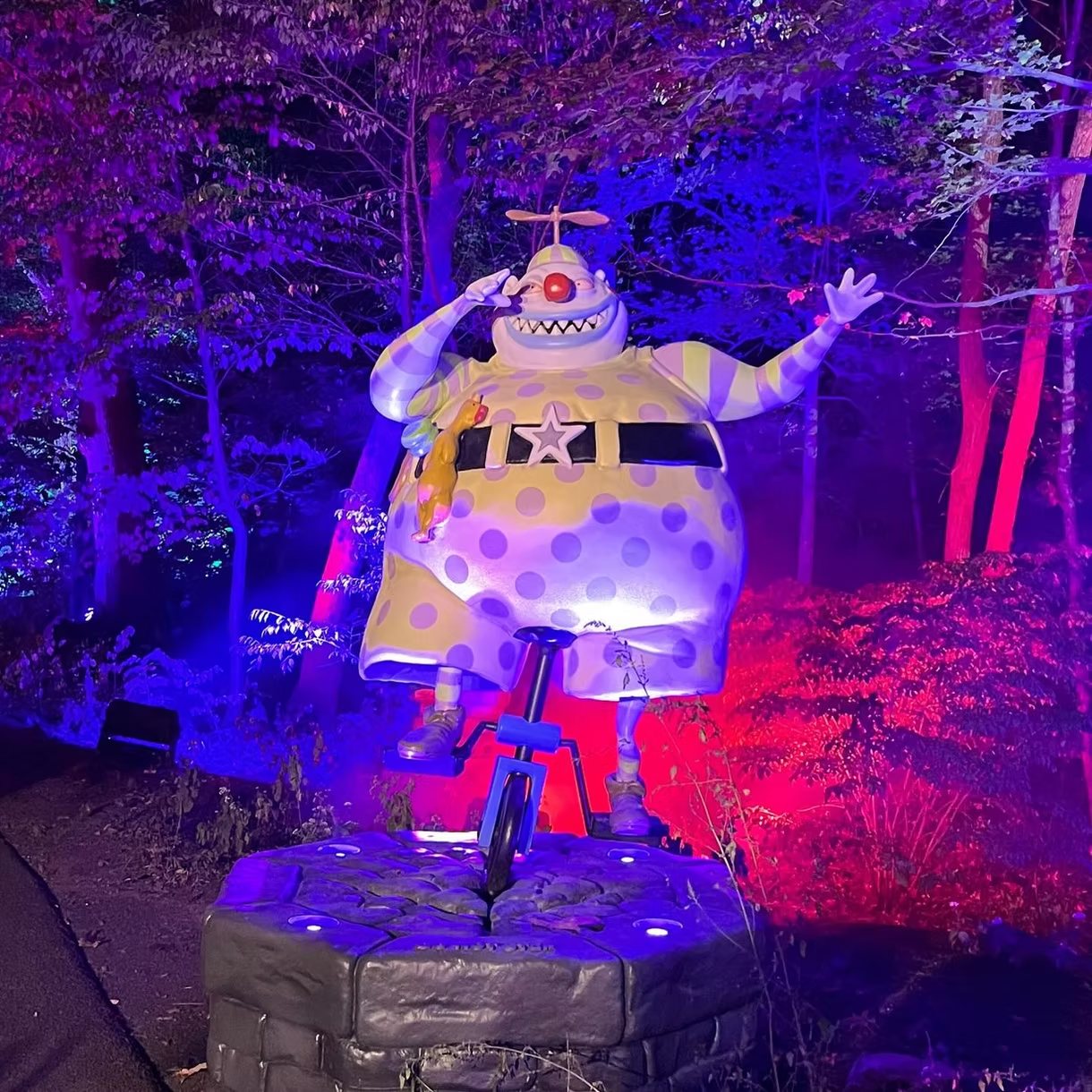 A giant polka-dot clown on a bicycle sculpture lit up at night