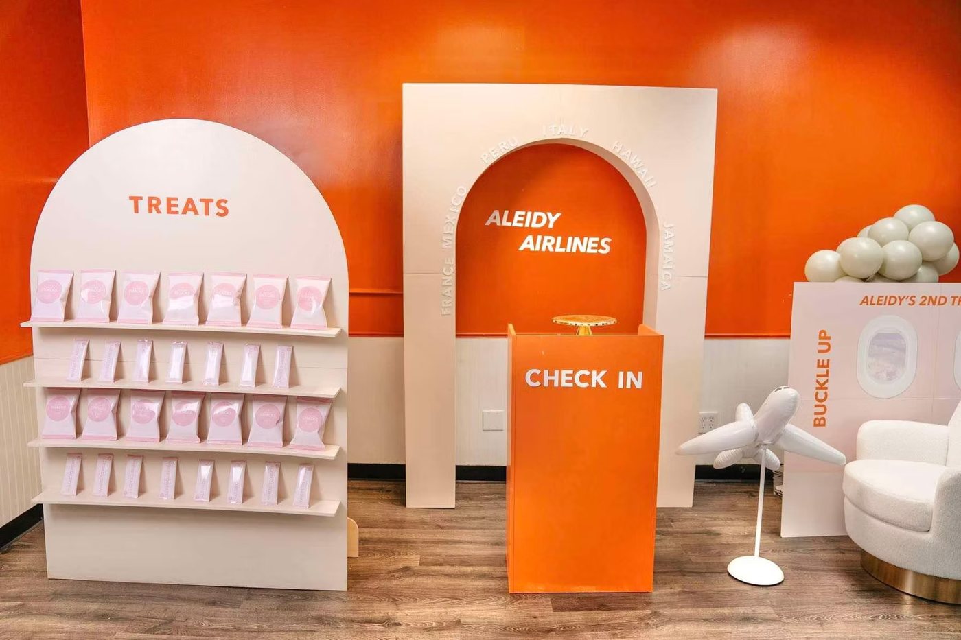 A bright orange pop-up with arched white shelving, a check-in desk and an airline-themed photo spot