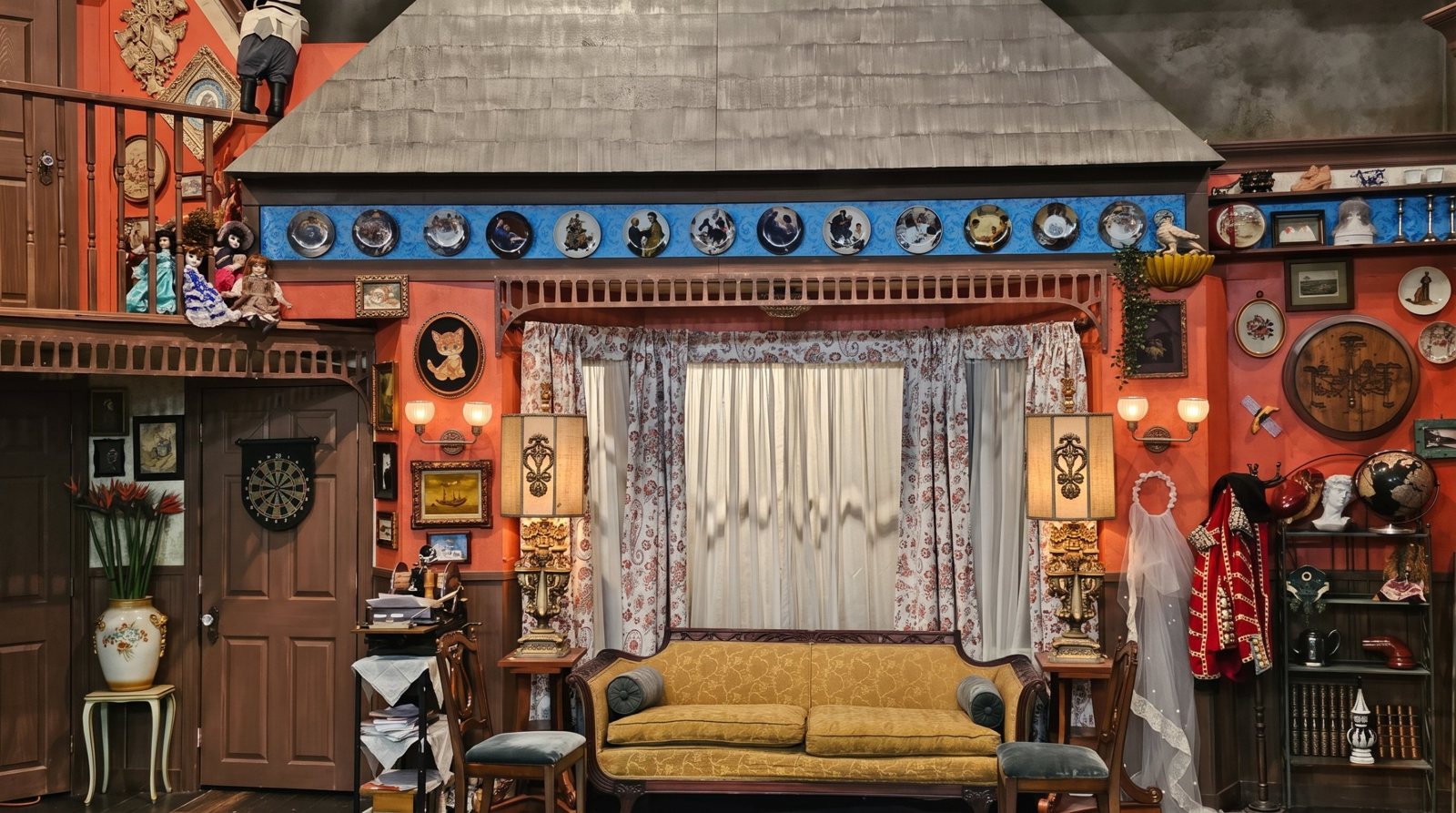 A cluttered, eclectic living-room TV set with an orange wall packed with frames and curios