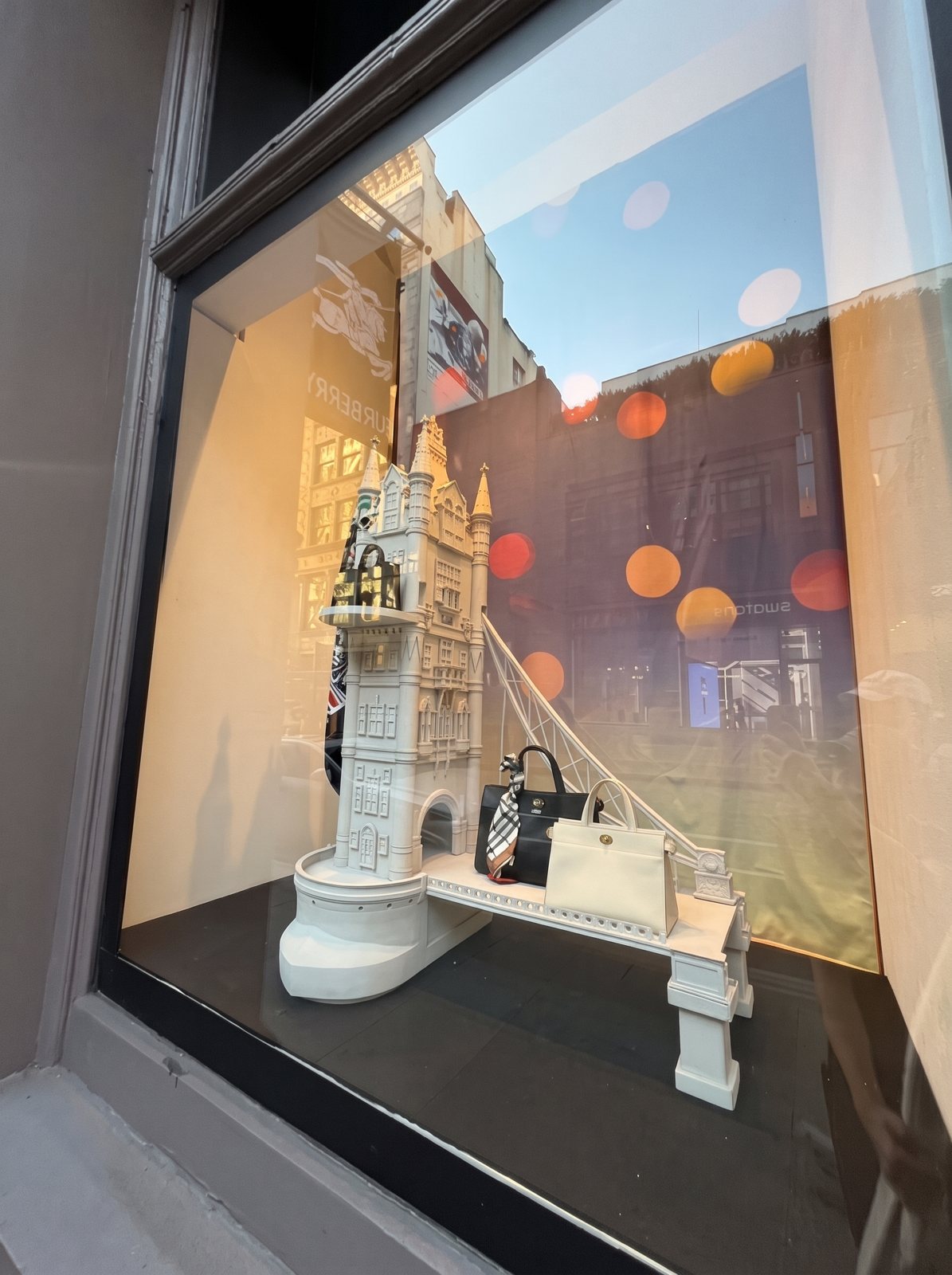 A close-up of a store window with a white sculpted clock tower and handbags