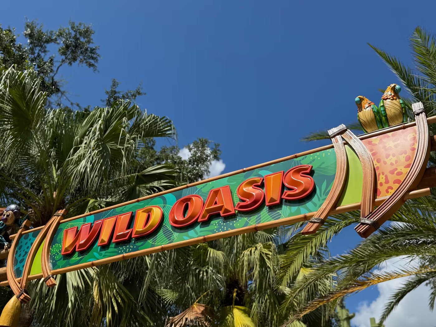 The Wild Oasis entrance arch sign with carved parrots against a blue sky