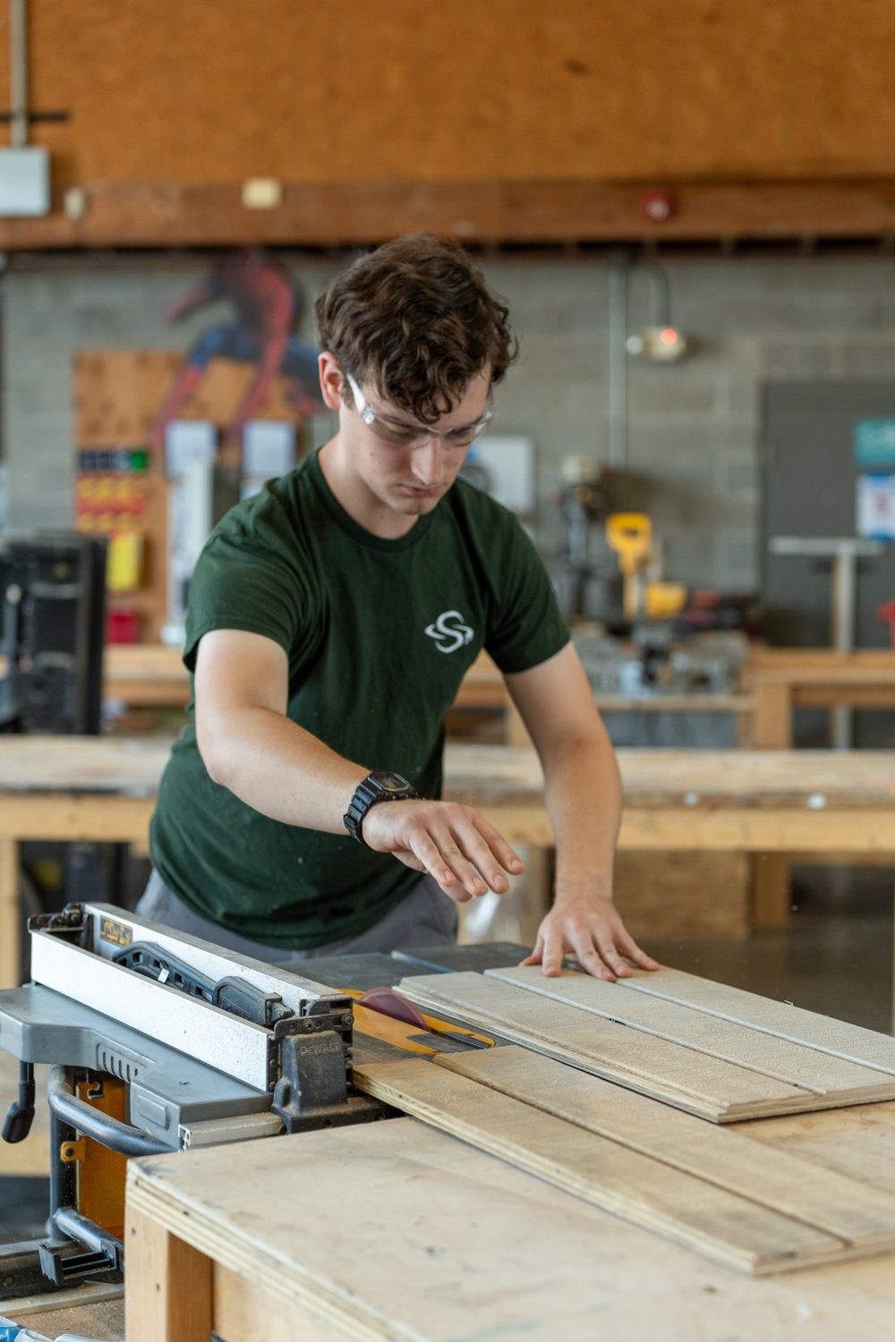 A carpenter in safety glasses ripping plywood on a table saw