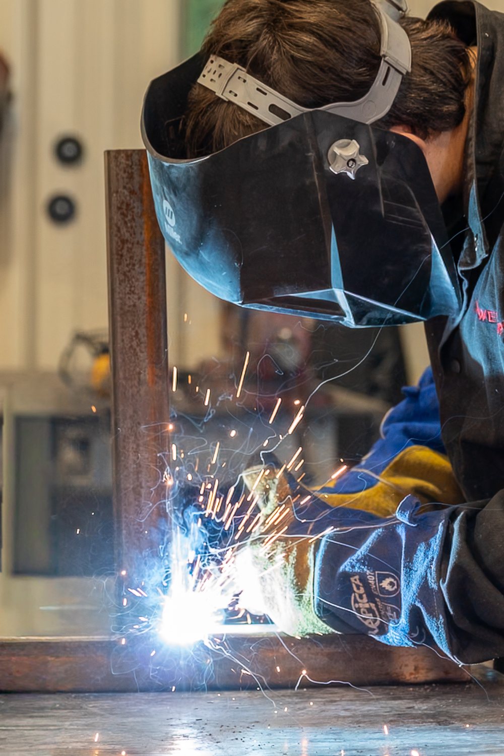 A welder in a helmet MIG welding a steel frame, sparks flying